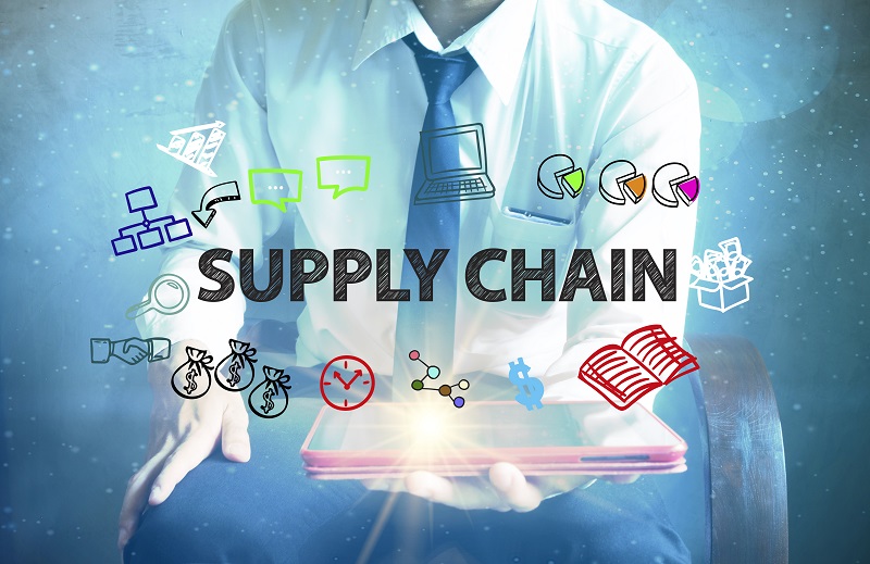 A businessman holding a tablet computer with "SUPPLY CHAIN" text and cartoon icons related to trade.